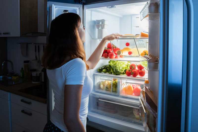 Photo of woman looking inside refrigerator.