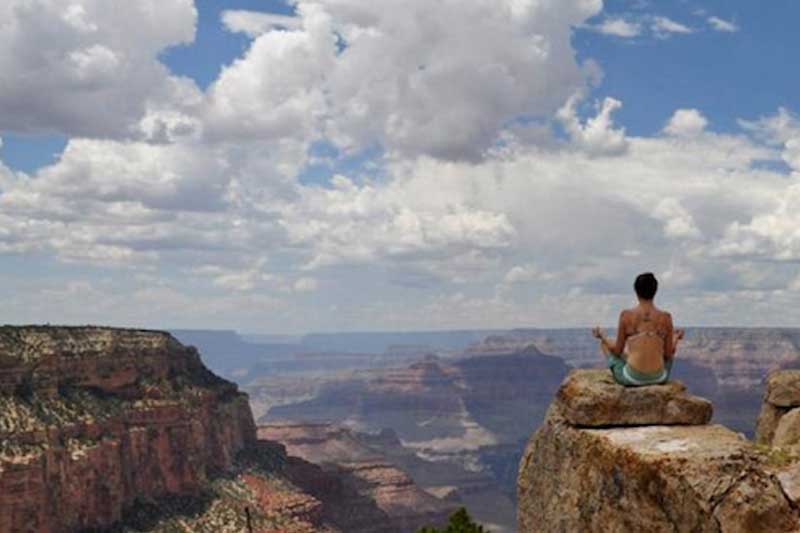 Photo of woman meditating on a cliff.