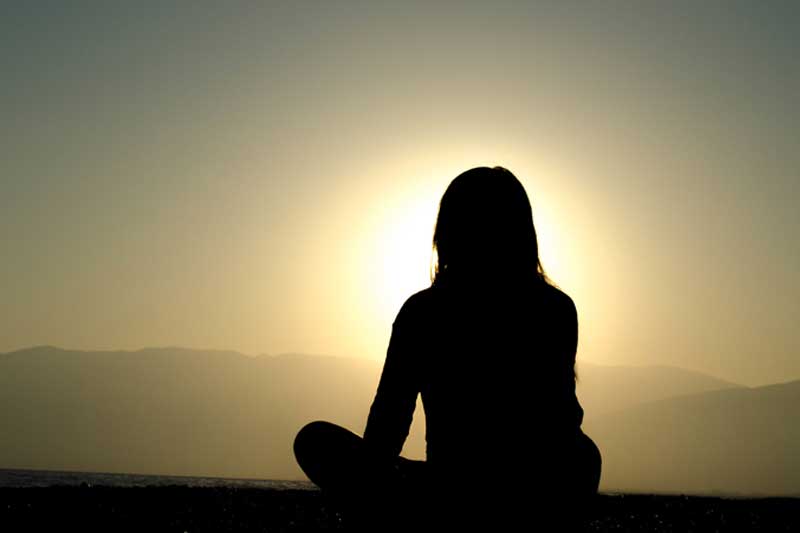 Photo of a woman meditating at sunset.