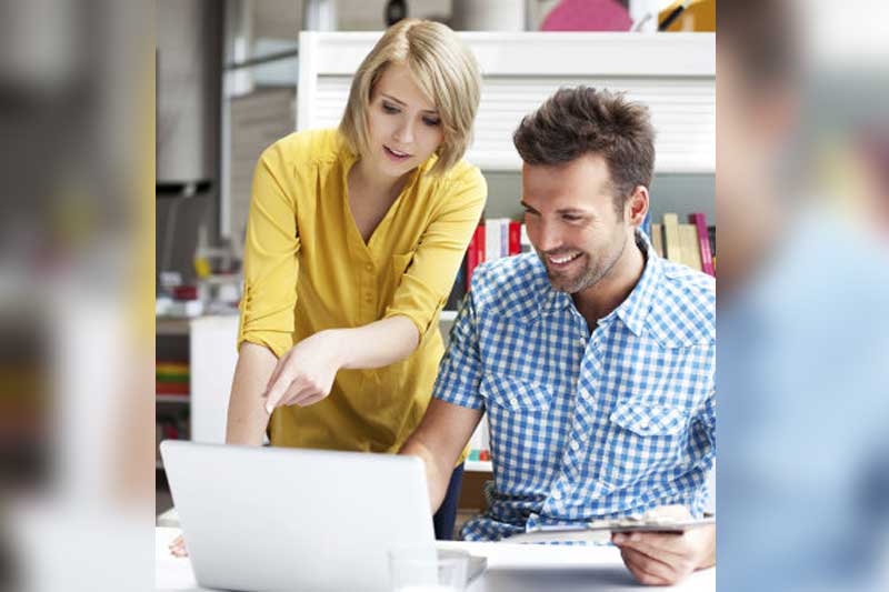 Photo of two employees discussing image on laptop.