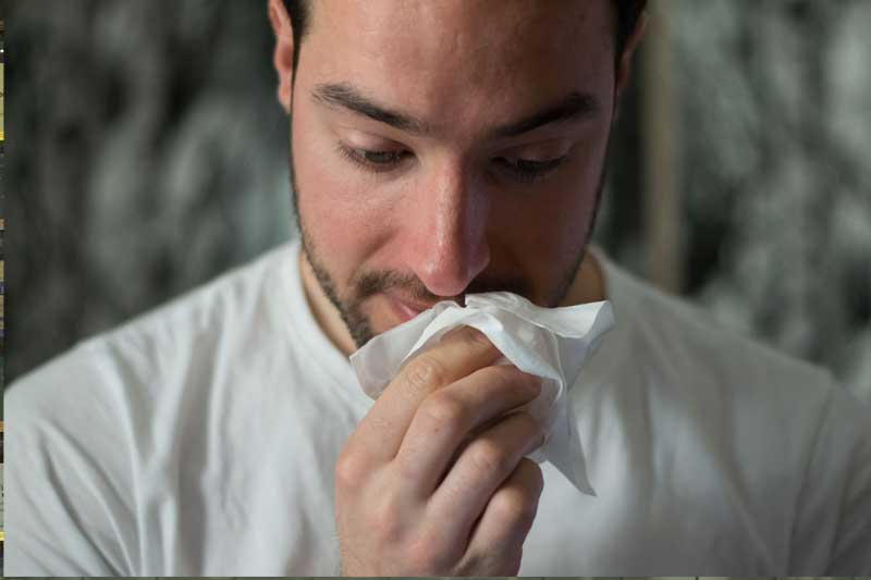 Photo of man with tissue blowing his nose.